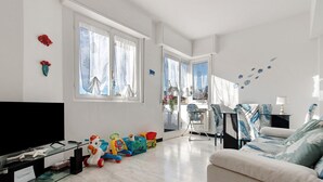 Ein großzügiges Wohnzimmer mit Flachbildfernseher, einer Couch, einer Essecke mit Tisch und Stühlen sowie einer Küchenzeile mit Herd und Schränken.