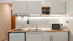 Una cocina compacta con armarios blancos, microondas integrado, fregadero y refrigerador pequeño.