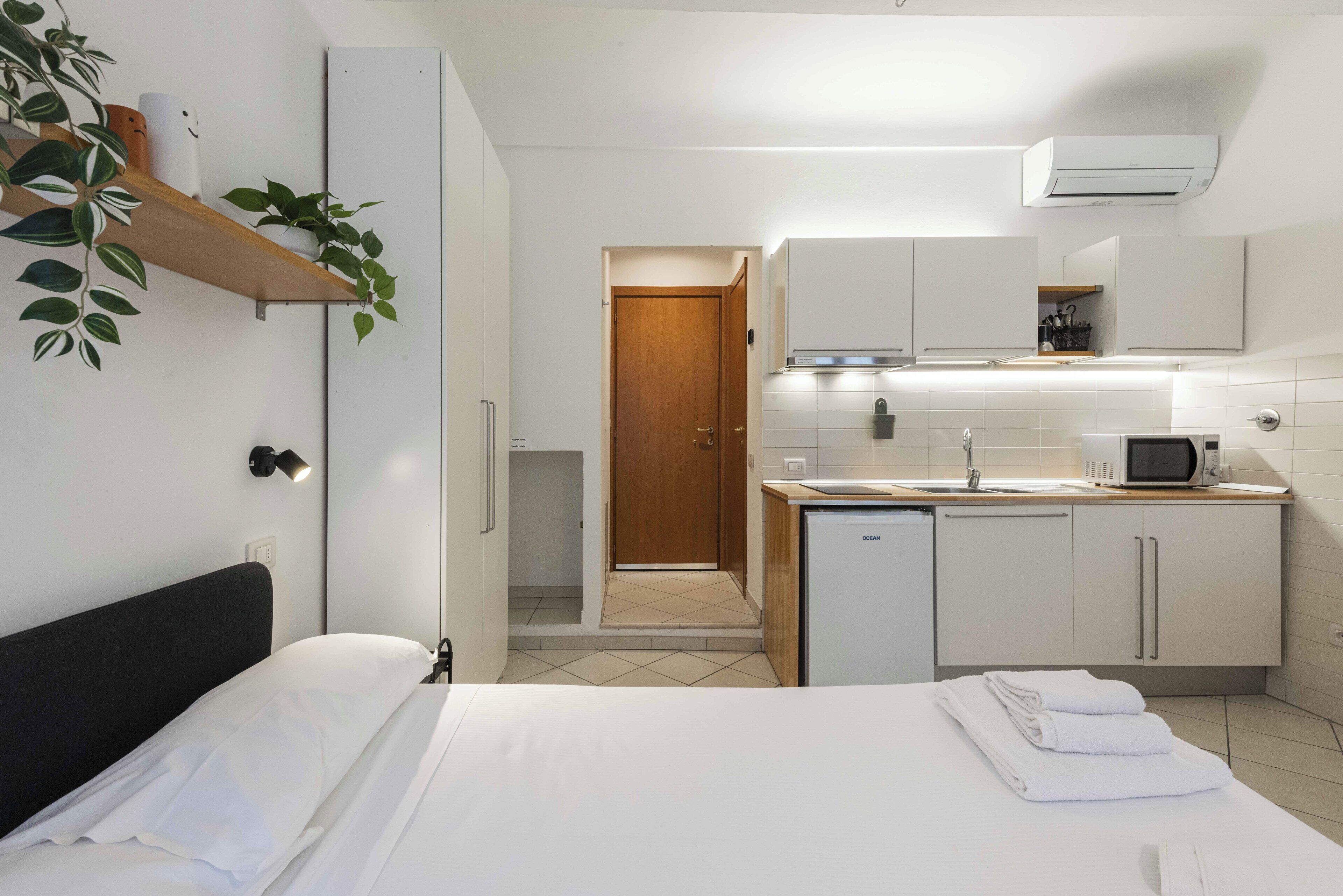 Een moderne hotelkamer met een bed, een kleine kitchenette en een houten deur naar een gang.