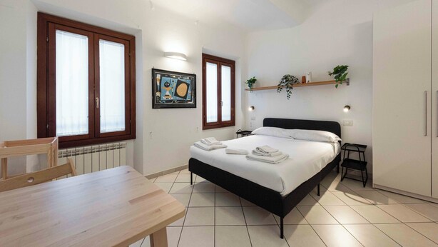 Un dormitorio con cama, una mesa de madera, una silla, un radiador y una ventana con persianas.