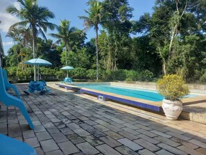 Une piscine dotée d’une terrasse carrelée, entourée de palmiers et agrémentée de quelques parasols.
