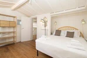 A bedroom with a bed, a wooden shelf unit, and a door leading to another room. - San Frediano Designer Duplex (Firenze)