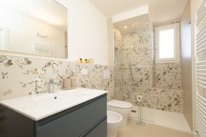 A bathroom with a white sink, dark cabinet, toilet, and shower with floral wallpaper. - San Frediano Designer Duplex (Firenze)