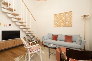 A modern living room with a staircase, a sofa set, a flat-screen TV, and decorative wall panels. - San Frediano Designer Duplex (Firenze)