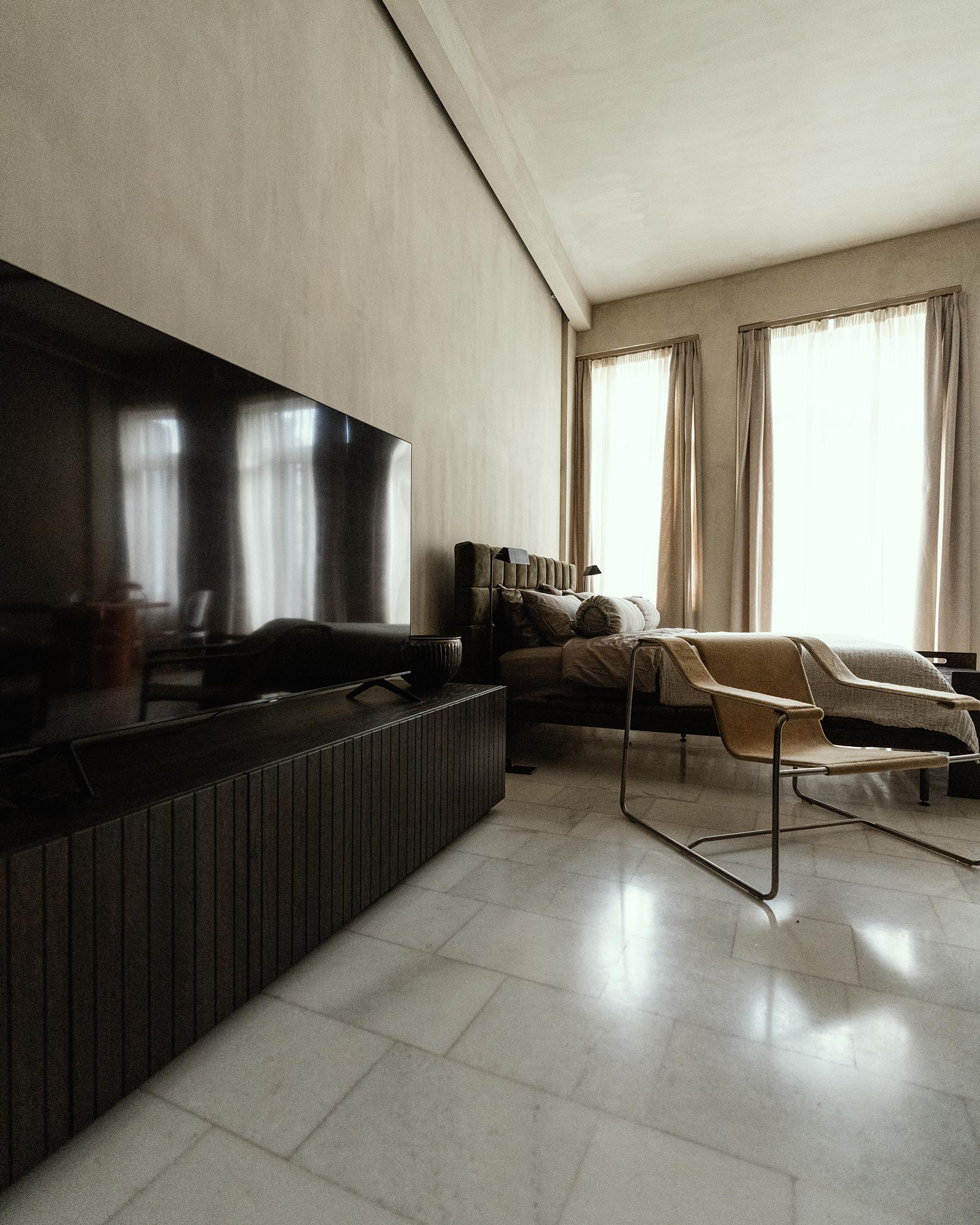 A modern living room with a large flat-screen TV, a dark wooden console table, a sofa, and a chair.