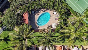 Vista aérea de un resort con piscina rodeada de palmeras y una cancha de tenis.