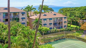 Un hotel de varios pisos con balcones, rodeado de exuberante vegetación y una cancha de tenis.
