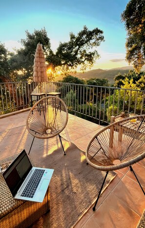 Un balcone con sedie in vimini, un tavolo e un computer portatile.