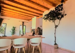 A modern interior with a wooden ceiling, a dining area with white chairs, a sofa, and a large potted plant. - Villa 'Õku' with Sea View, Wi-Fi and Air Conditioning (Rincovo)