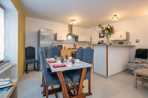 A modern kitchen with a dining area, a built-in oven, and a small island with a vase of flowers.