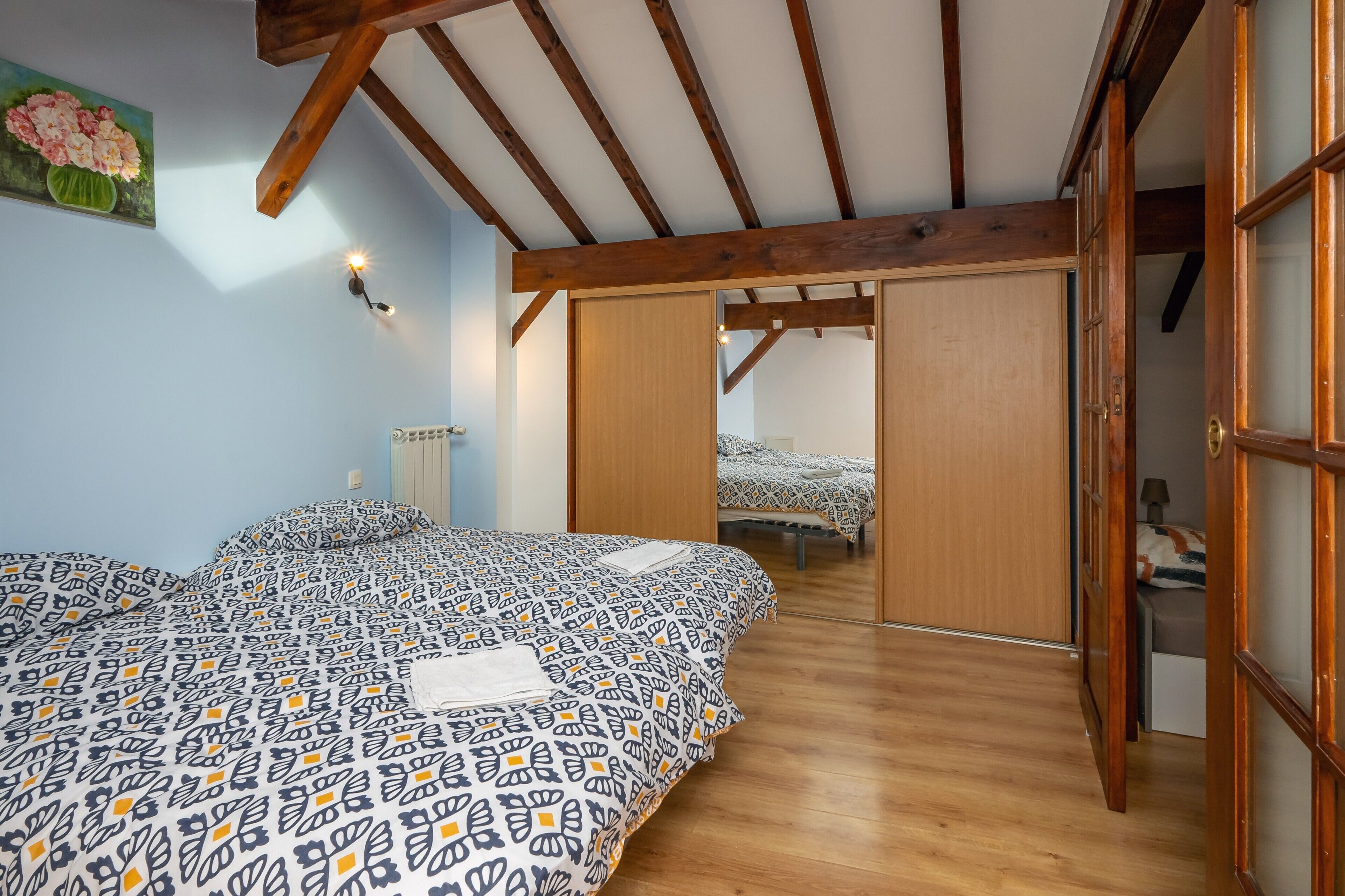 A bedroom with a bed, wooden beams, a sliding door, and a painting on the wall.