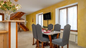 Ein Essbereich mit Holztisch und -stühlen, einer Blumenvase, einem an der Wand montierten Fernseher und einer Treppe im Hintergrund.