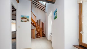 Ein schmaler Flur mit einer Holztreppe, weißen Wänden und gefliestem Boden.