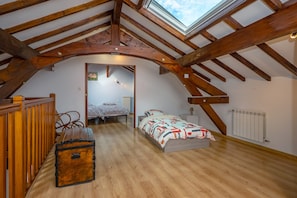 A loft bedroom with a sloped ceiling, wooden beams, a skylight, a bed, a chest of drawers, and a radiator.
