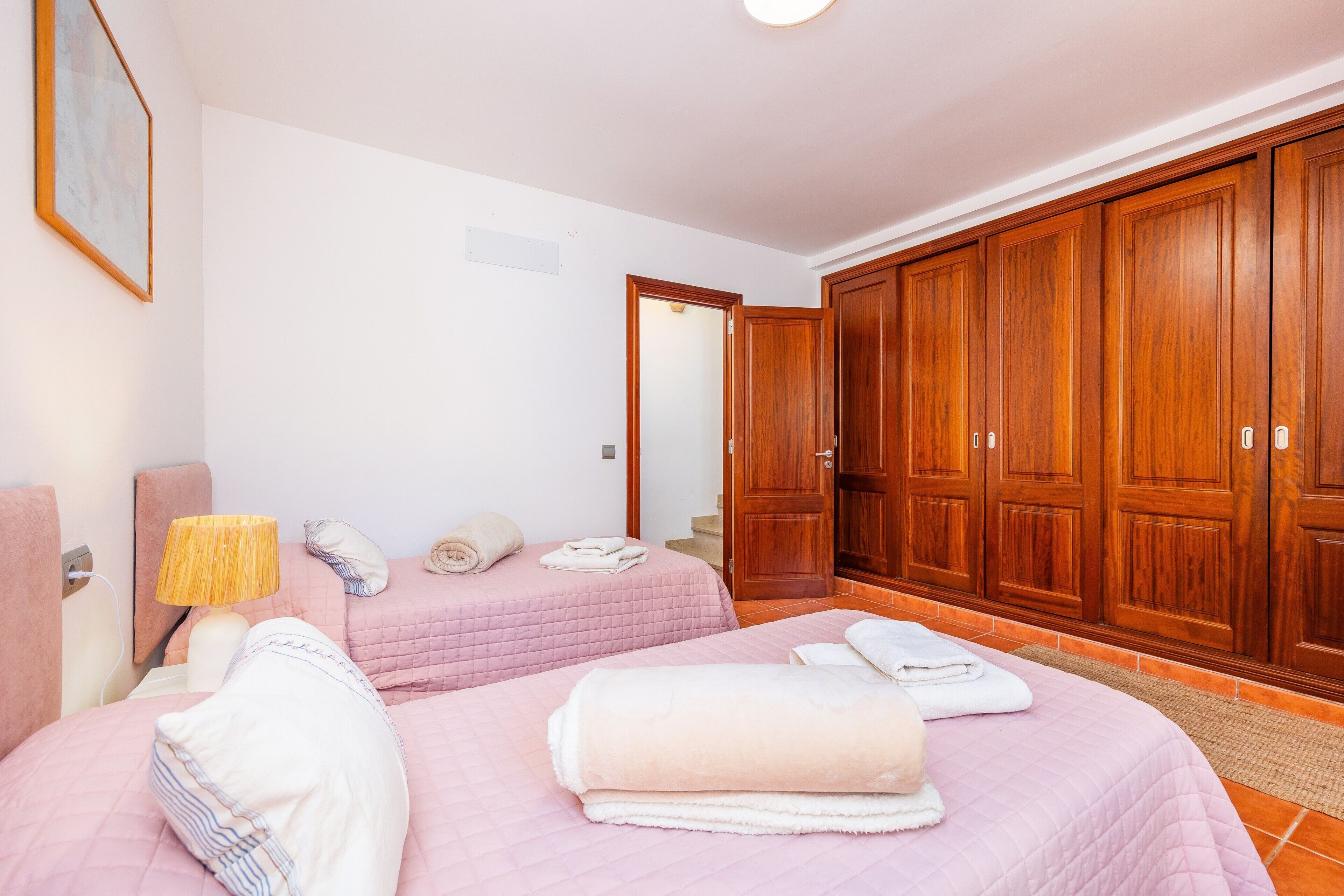 Ein Hotelzimmer mit zwei Betten, einem Holzschrank, einer Nachttischlampe und einem gerahmten Bild an der Wand.
