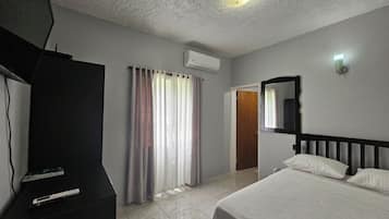 Ein Hotelzimmer mit Bett, Fernseher, Vorhängen, Spiegel und Deckenleuchte.