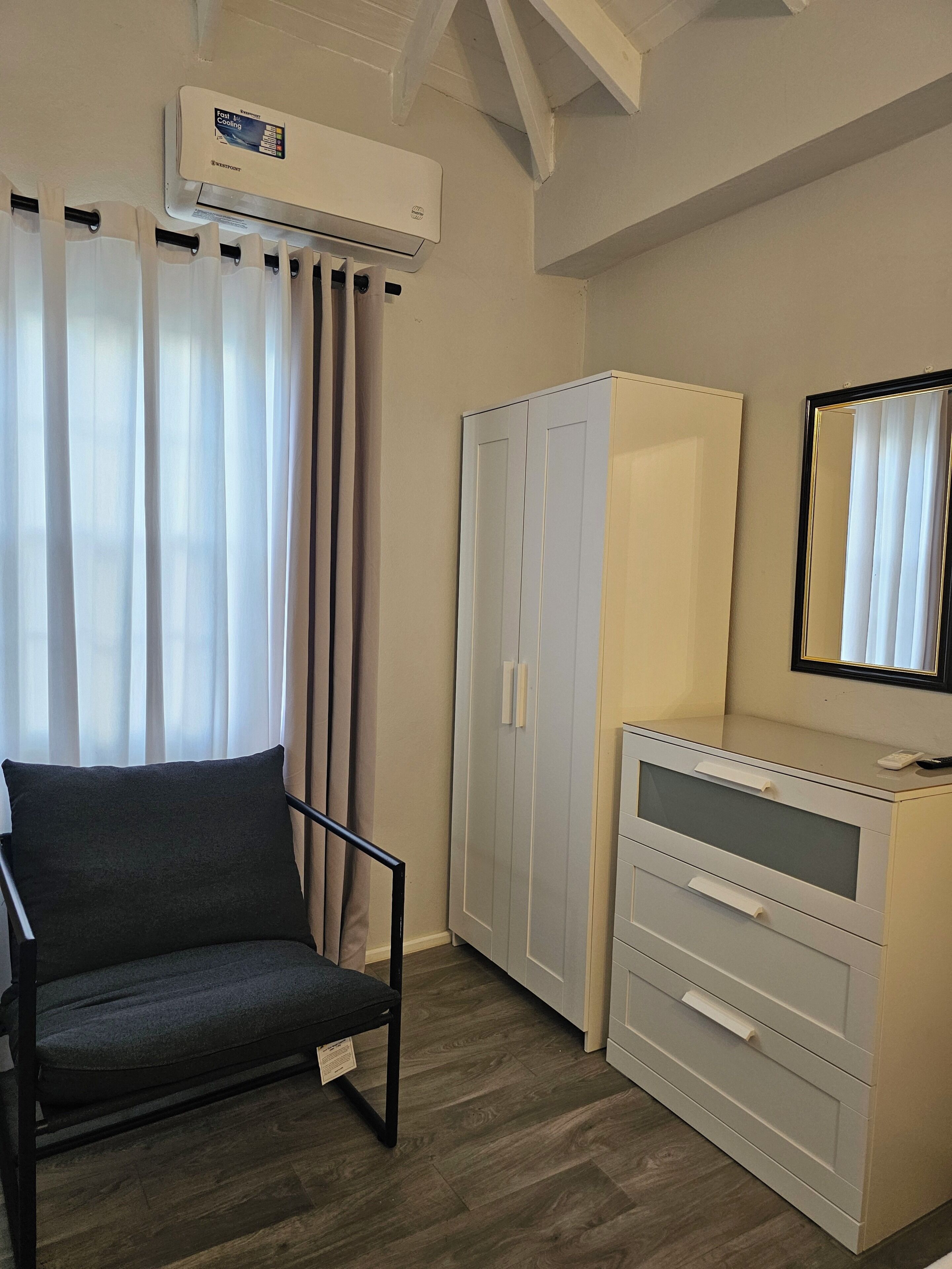 Una habitación con una silla, armario, espejo y equipo de aire acondicionado.
