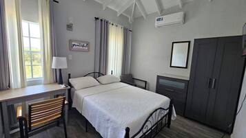 A bedroom with a bed, a desk, a chair, a wardrobe, and a window with curtains.