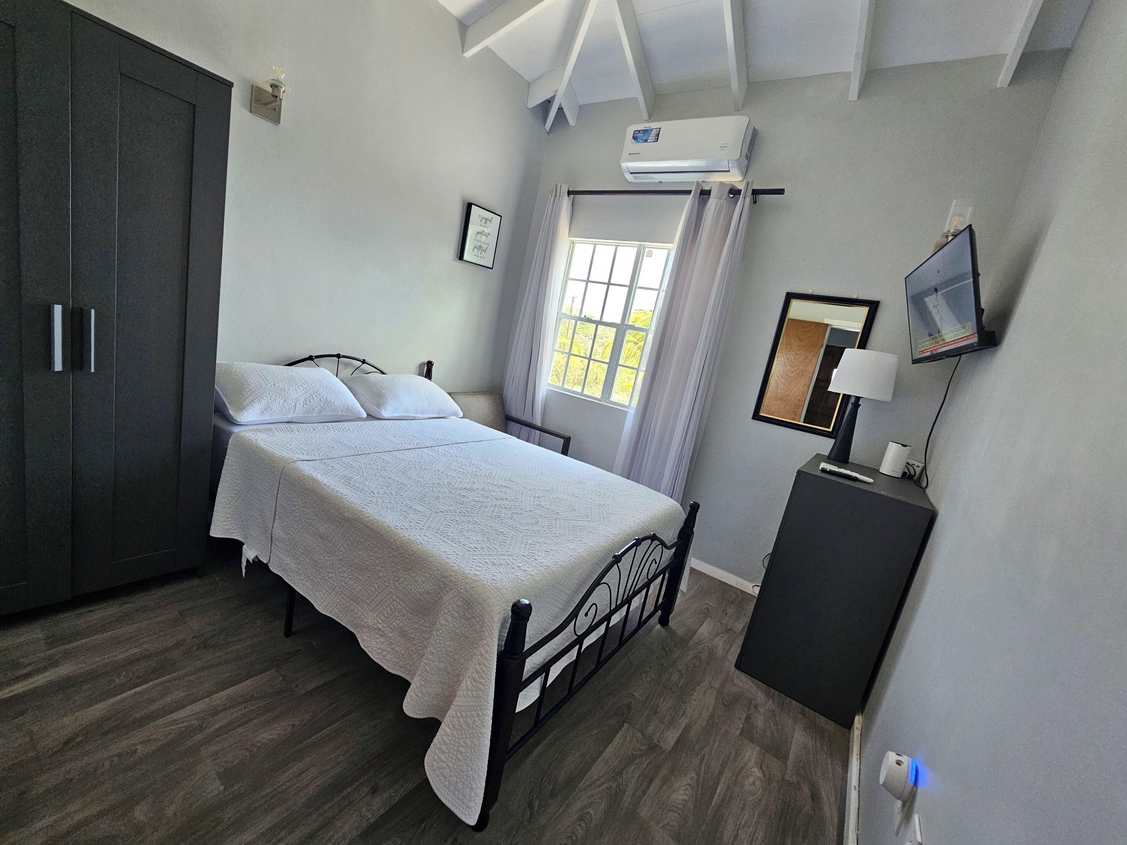 Une chambre à coucher comprenant un lit, une armoire, un téléviseur et un appareil de climatisation.