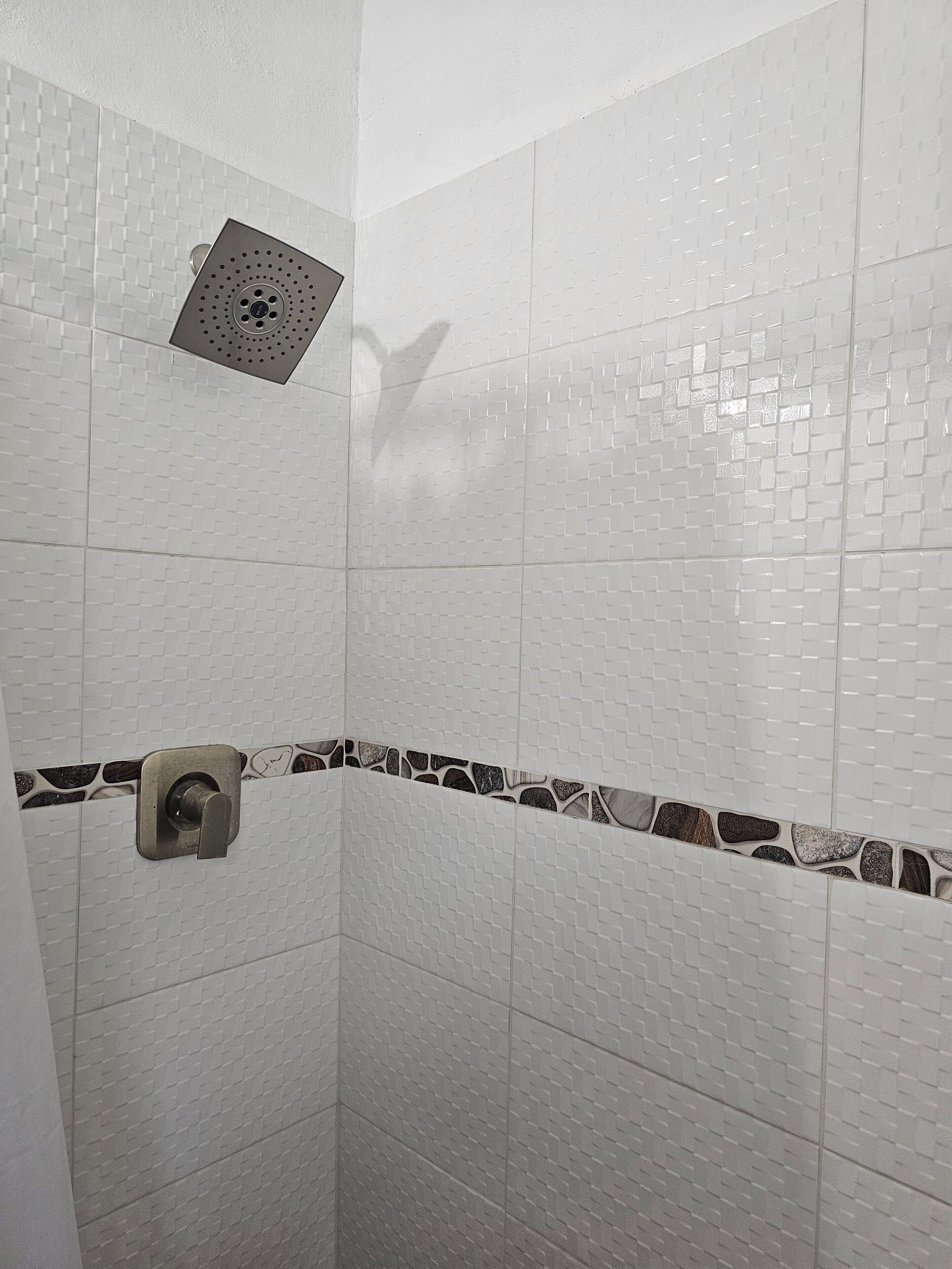 Een douche met witte betegelde wanden, een douchekop en een decoratieve rand van steen.