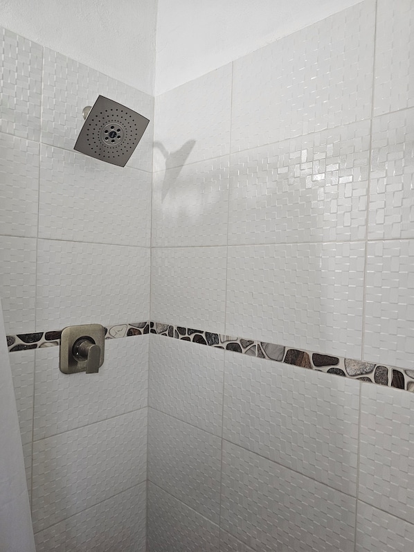 A shower with white tiled walls, a showerhead, and a stone accent border. - Anne's Apartments (Osbourn)