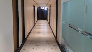 A long, narrow hallway with a marble floor and glass walls on one side. - Januson Hotel (Gandhinagar)