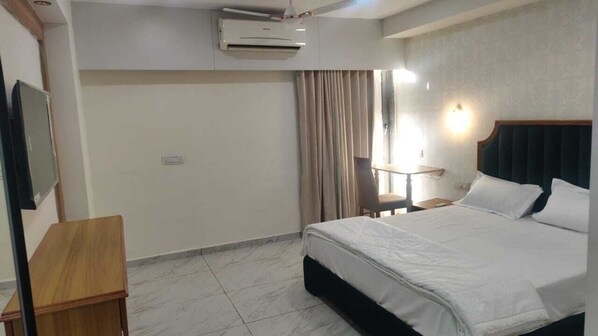 Una habitación de hotel con cama, escritorio, aire acondicionado, silla y ventana con cortinas.