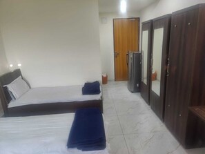 A hotel room with two single beds, a wardrobe, a refrigerator, and a door. - Januson Hotel (Gandhinagar)