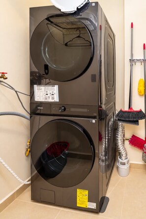 A stacked washer and dryer unit with a control panel, hoses, and a mop on the right side. - Huayacán cozy apartment + Gym + Rooftop + Pool (Cancún)