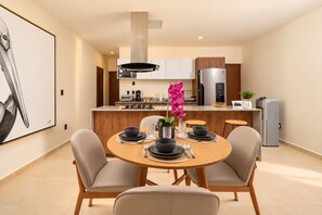 A modern kitchen with a central island, stainless steel appliances, and a dining area with a round table and chairs. - Huayacán cozy apartment + Gym + Rooftop + Pool (Cancún)