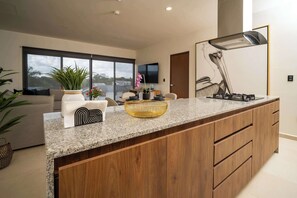 Eine moderne Küche mit Granitarbeitsplatte, Holzschränken, einem großen Fenster und einem an der Wand befestigten Flachbildfernseher.