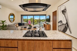 A modern kitchen with a central island, a dining area with a round table, and a large window offering a view of the outdoors. - Huayacán cozy apartment + Gym + Rooftop + Pool (Cancún)