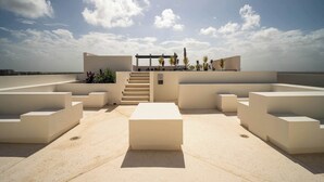 Eine Dachterrasse mit minimalistischem Design, mit einer zentralen Sitzecke, einer Treppe und einer Pergola mit Pflanzen.
