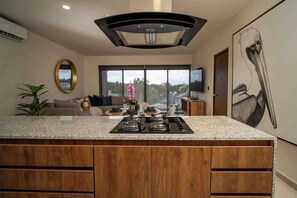 A modern kitchen with a granite countertop, wooden cabinets, and a built-in stove. - 2BR  Stylish Retreat | Rooftop Pool & Huayacán (Cancún)