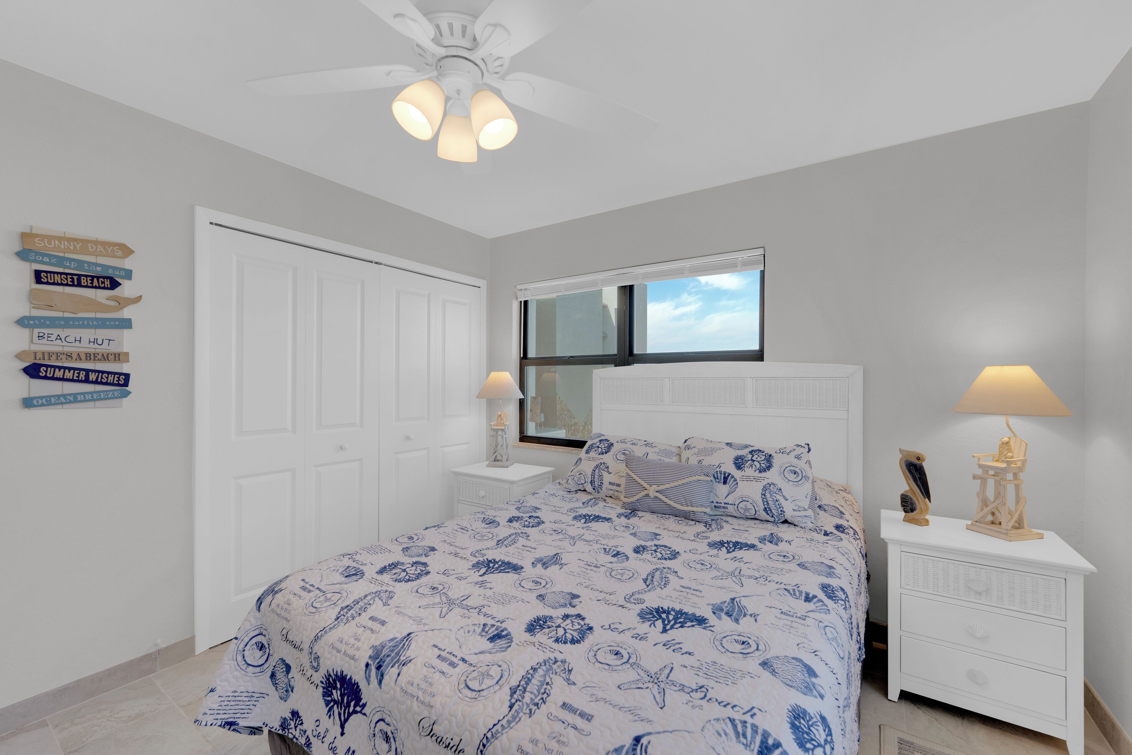 A bedroom with a bed, nightstands, a ceiling fan, a window, and wall decorations.