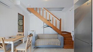 Un espacio habitable pequeño con una escalera de madera, un sofá, una mesa de comedor y un refrigerador.