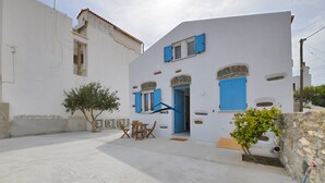 Un edificio blanco con contraventanas azules y un pequeño patio con mesa y sillas.