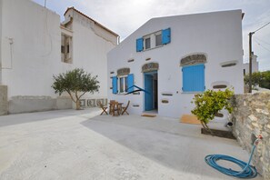 A white building with blue shutters and a small patio area with a table and chairs. - Villa Antika, very close to the shops and restaurants in Korissia, Kea. (Coressia)