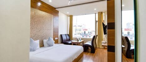 A hotel room with a bed, a desk, a chair, and a view of the city through the window.