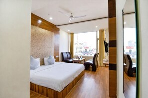 A hotel room with a bed, a desk, a chair, and a view of the city through the window. - Hotel Black Diamond (Zirakpur)