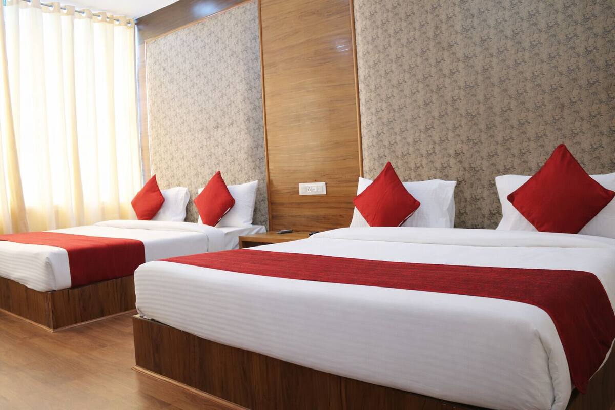 A hotel room with two single beds and one double bed, each with red and white bedding.