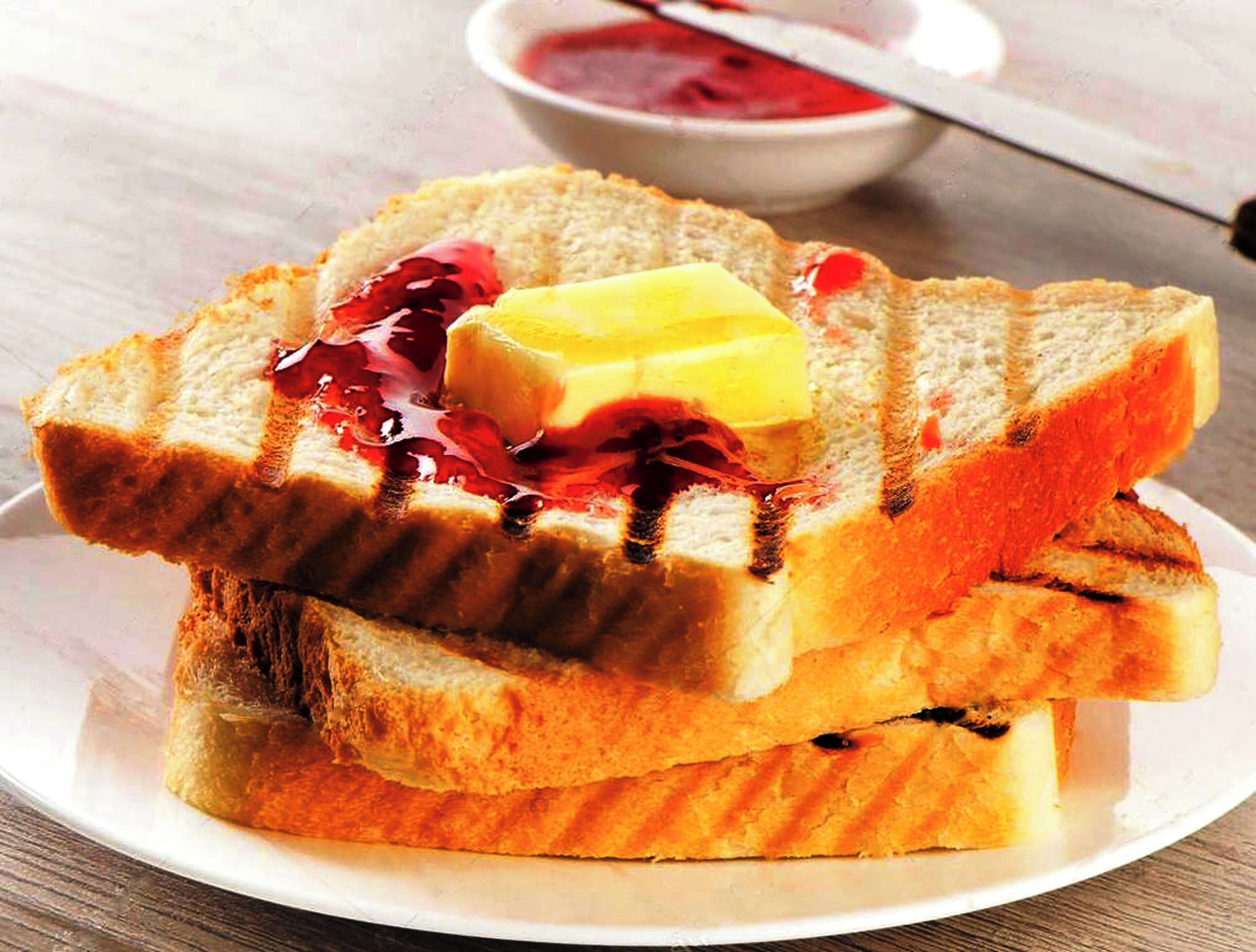 Two slices of toast with butter and jam on a white plate.