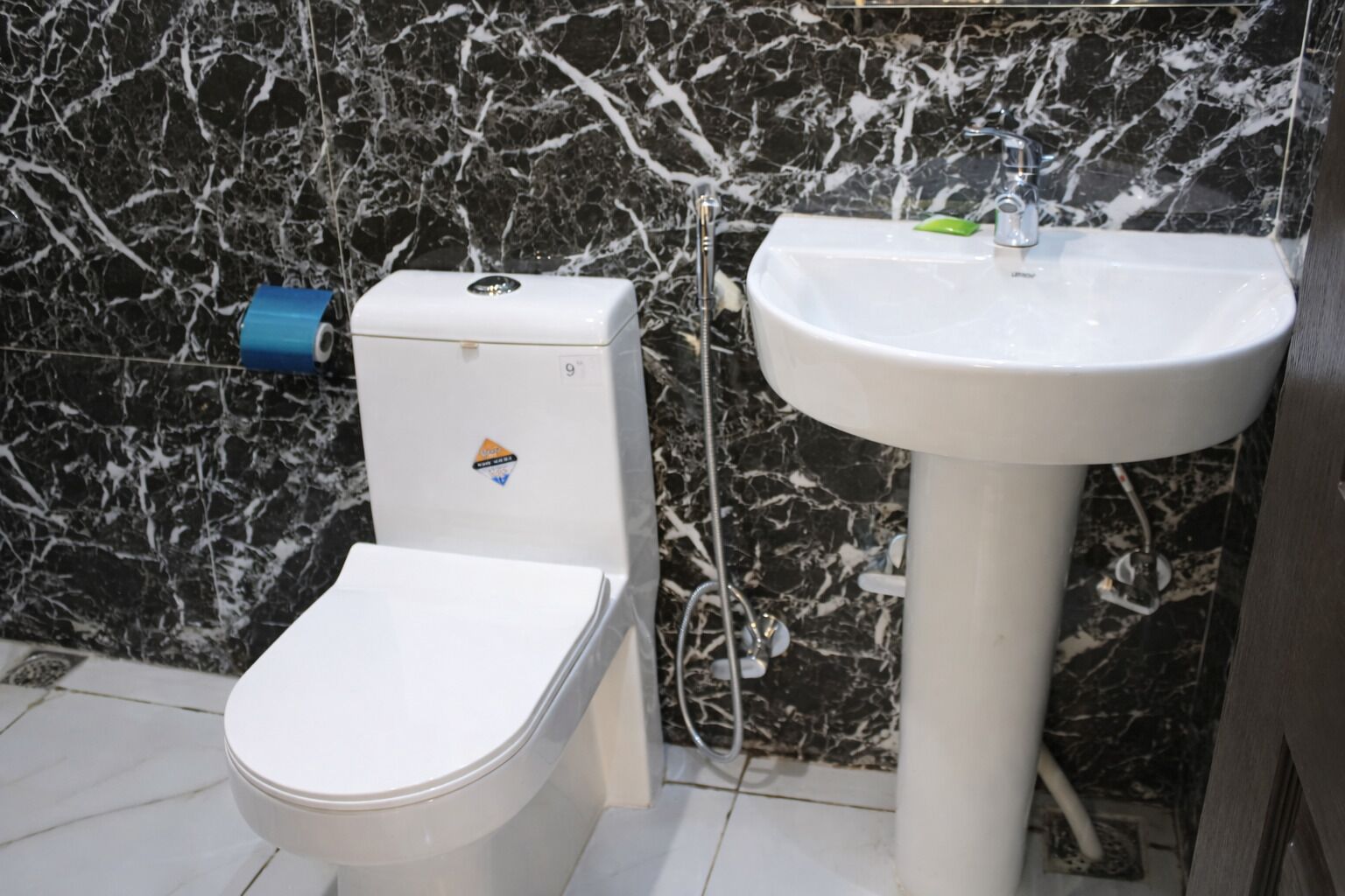 Et badeværelse med toilet og håndvask opført mod en marmorvæg.