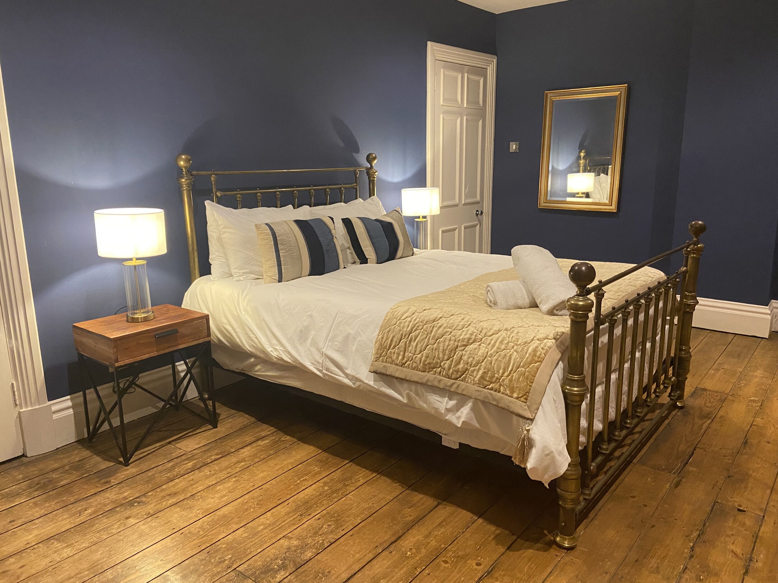 A bedroom with a bed, nightstands, a mirror, and a door.