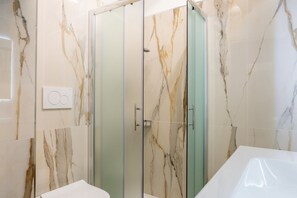 A bathroom with a glass-enclosed shower, marble walls, and a white sink. - Orsanmichele Suite - Florence (Firenze)