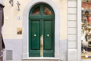 A green double door with a white frame, a small window above it, and a doorbell above the door. - Orsanmichele Suite - Florence (Firenze)