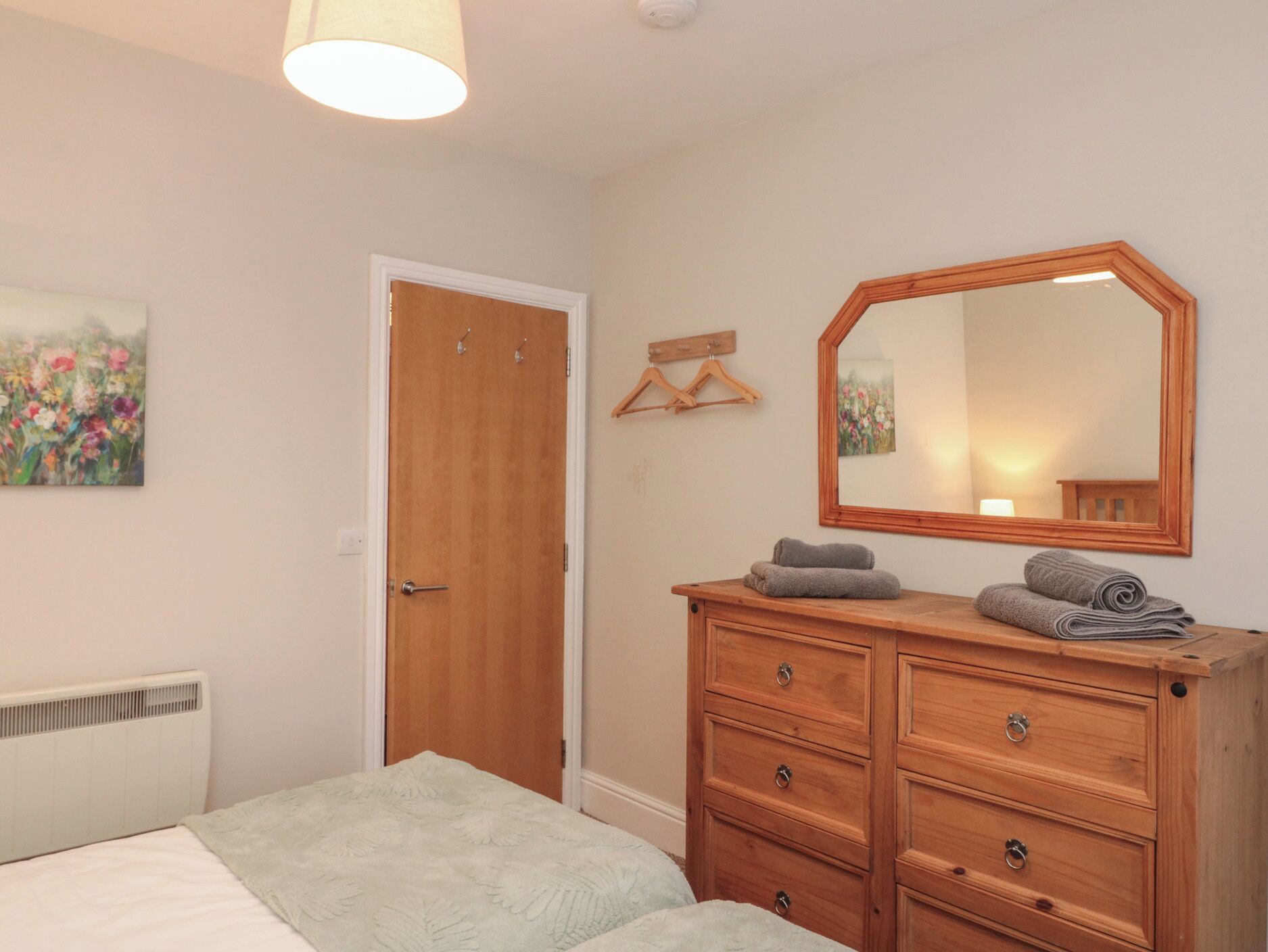 A bedroom with a bed, a dresser, a mirror, a door, and a radiator.
