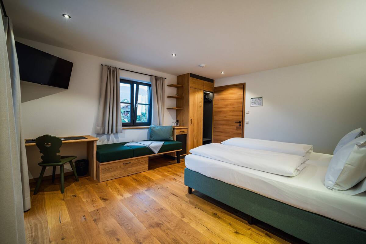 A modern bedroom with a bed, desk, chair, and a TV mounted on the wall.