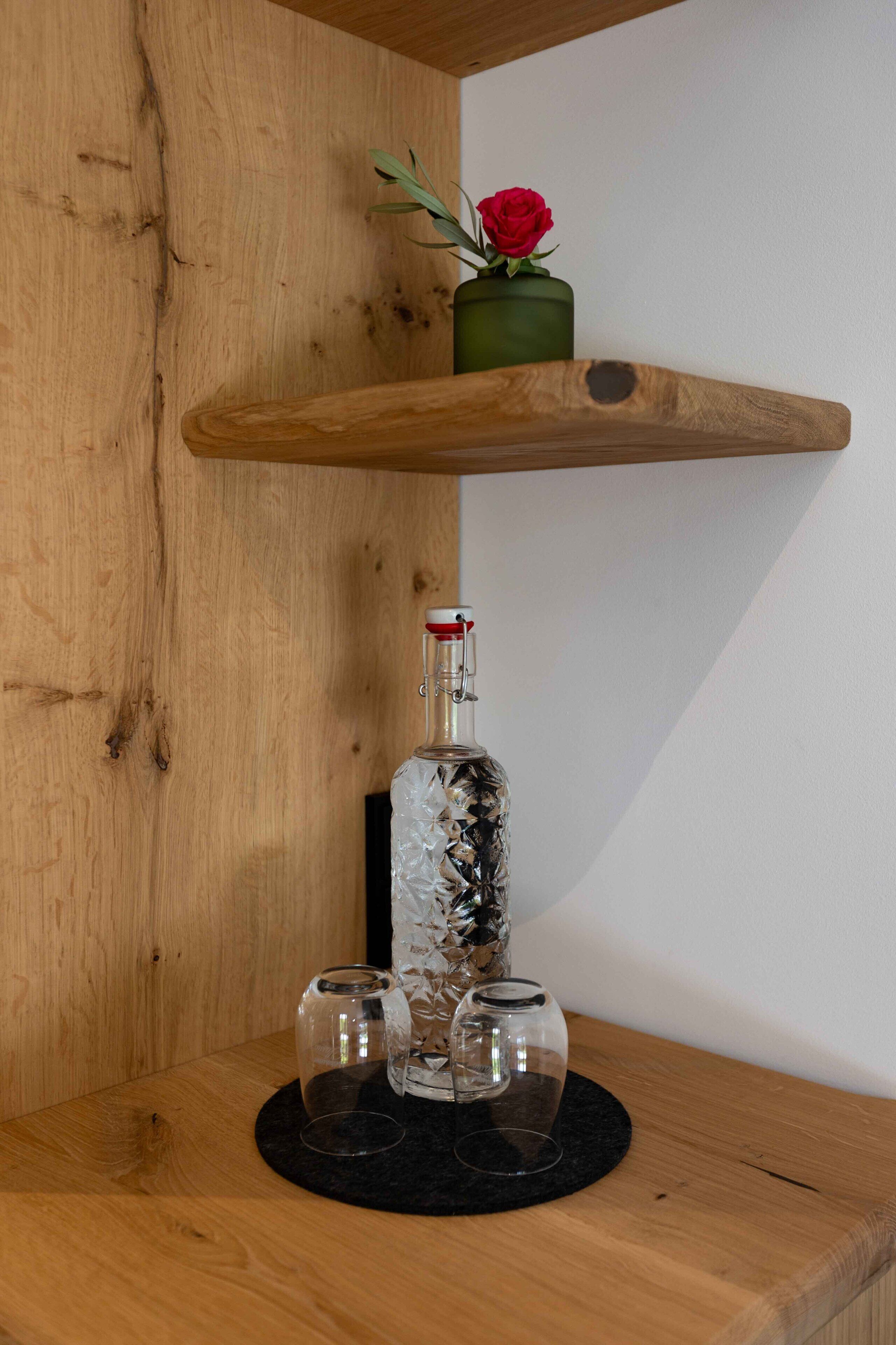 Ein Holzboden mit einer Glasflasche, zwei Gläsern und einer roten Rose in einem grünen Topf.