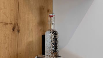 Ein Holzboden mit einer Glasflasche, zwei Gläsern und einer roten Rose in einem grünen Topf.